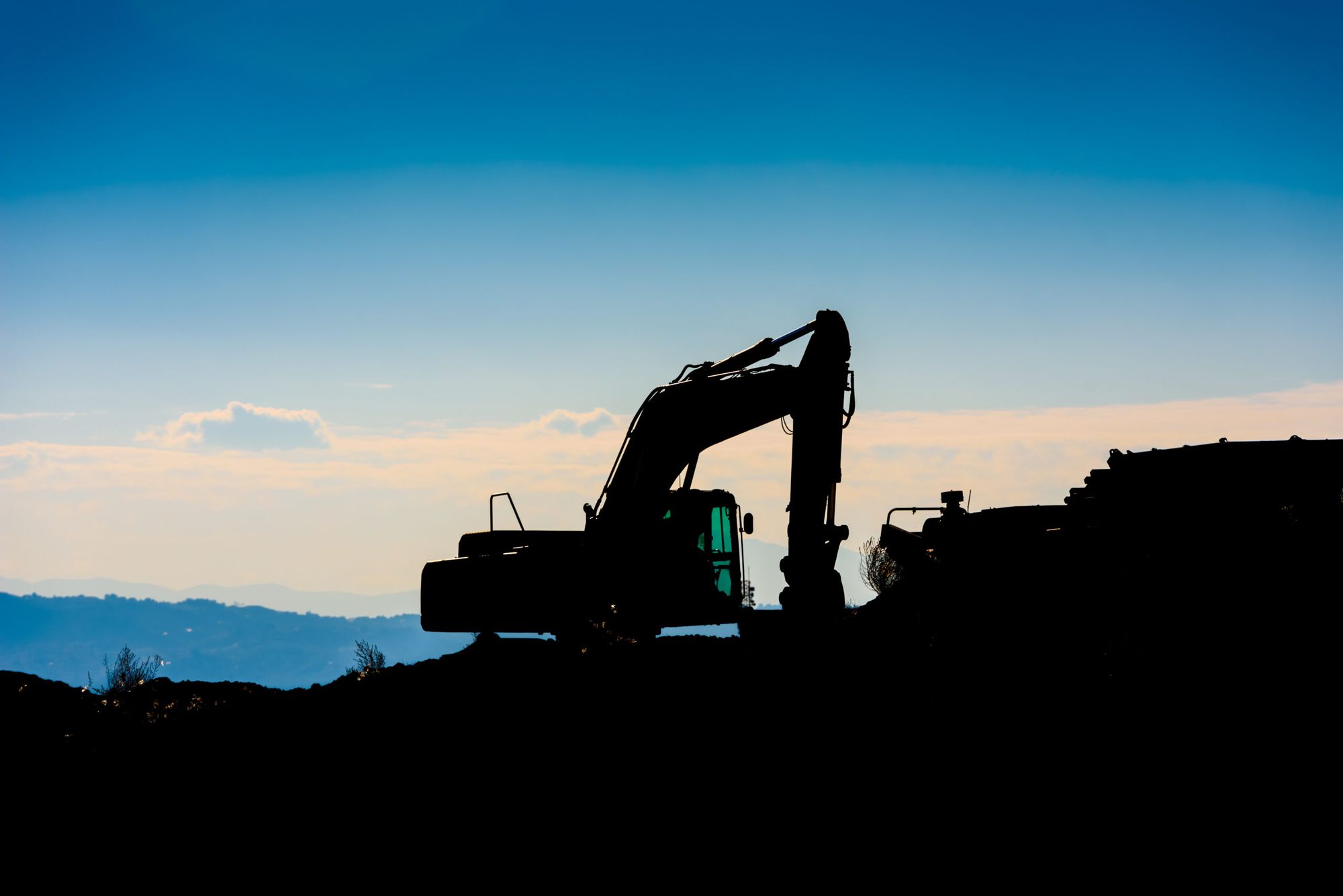 Excavator silhouetted on a hilltop at sunset